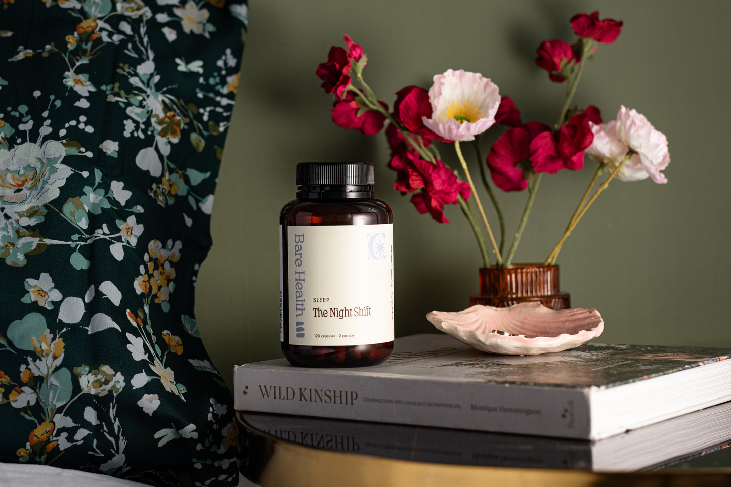 Bottle of 'Basic Health' on a stack of books with flowers and a shell in the background