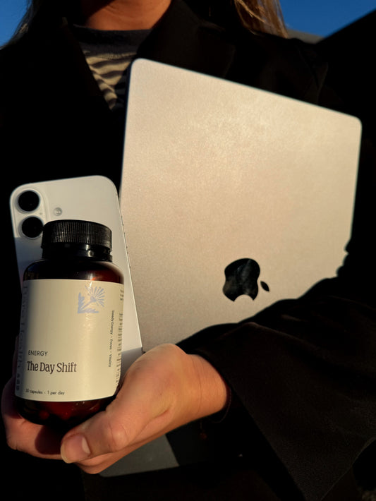 Person holding laptop and bottle of the day shift energy supplement