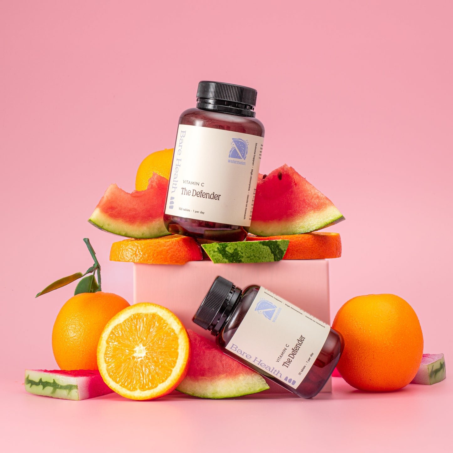 Two bottles of a product on a pink background with slices of watermelon, orange, and other fruits.